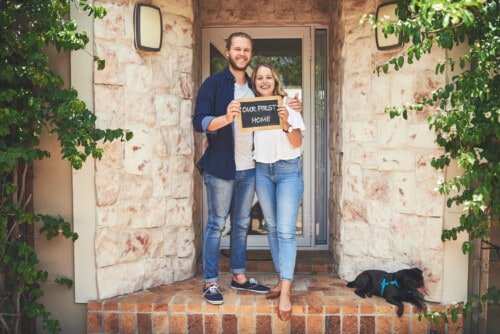 Portrait of a young couple holding a chalkboard with "our first home" written on it